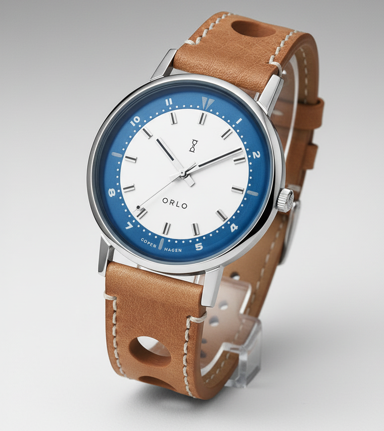 A silver-toned watch with a blue dial, camel-colored leather strap, and a silver caseback. The watch has a classic design with a simple, elegant appearance.